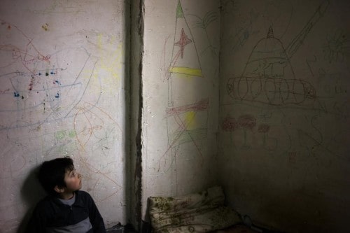 Iraq / IDP / Sadar, 7, leans against a wall covered in drawings, including a tank. His 10 member family, who had escaped Sinjar, live in this one room inside an unfinished building in Zakho. When I asked who had created all of these drawings, almost everyone pointed at Sadar who smiled happily. He was suffering from skin infection due to bad hygiene in the building, but his parents made sure they would keep him as clean as possible - a hard task to do when it's near freezing and not enough kerosene or wood to heat up the water. Daben City is a housing estate with five buildings once filled with more then 7000 Yazidi IDP's in Zakho. Now a few hundred are left fearful when and where they will be moved to while still facing multiple dangers including the cold, falling from floors or staircases or being hit by debris. The rest of the IDP's have started to be relocated since the middle of November. D. NAHR / February 2015