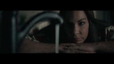 Still from Ashgrove, a woman staring at a running tap