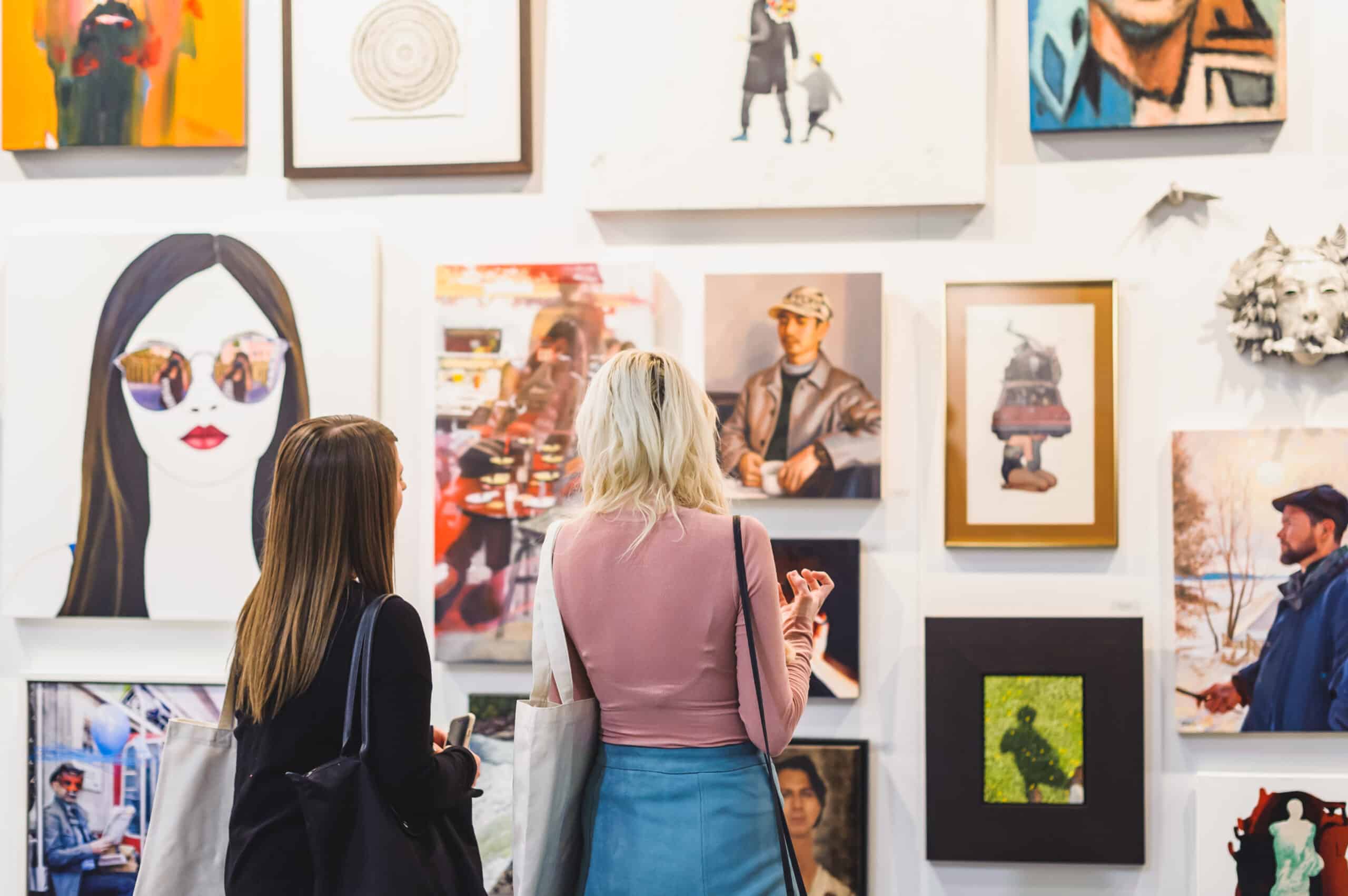 Two women stand in front of a wall of art.