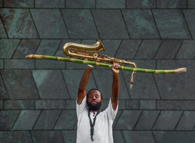 Jerome Ellis raises a saxophone and bamboo shoot over his head.