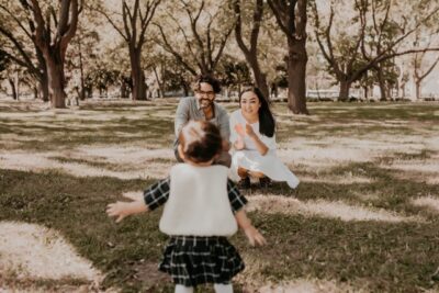 A young girl walking towards her parents in a park